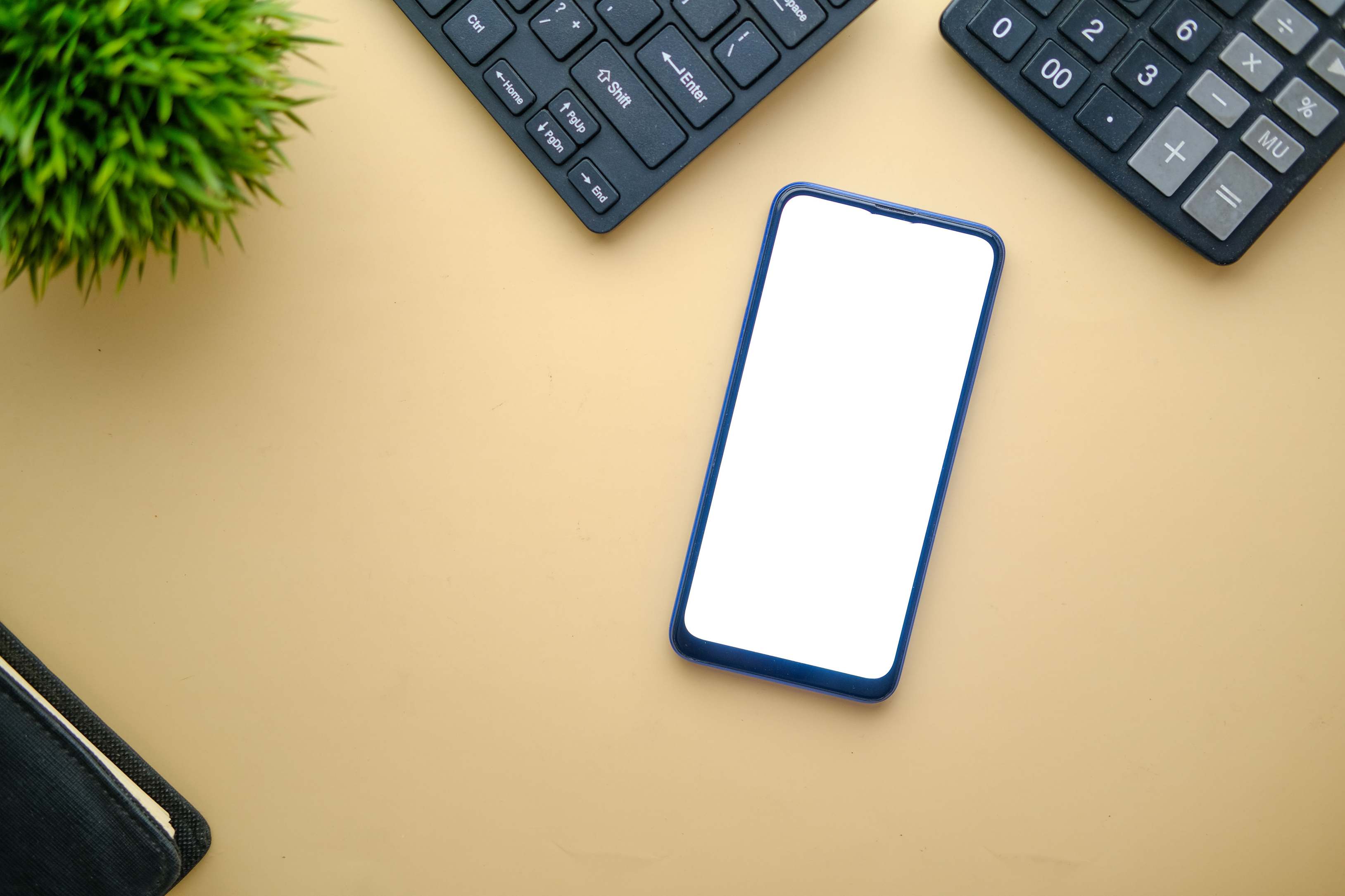 Overhead view of a smartphone on a desk with keyboard and plant