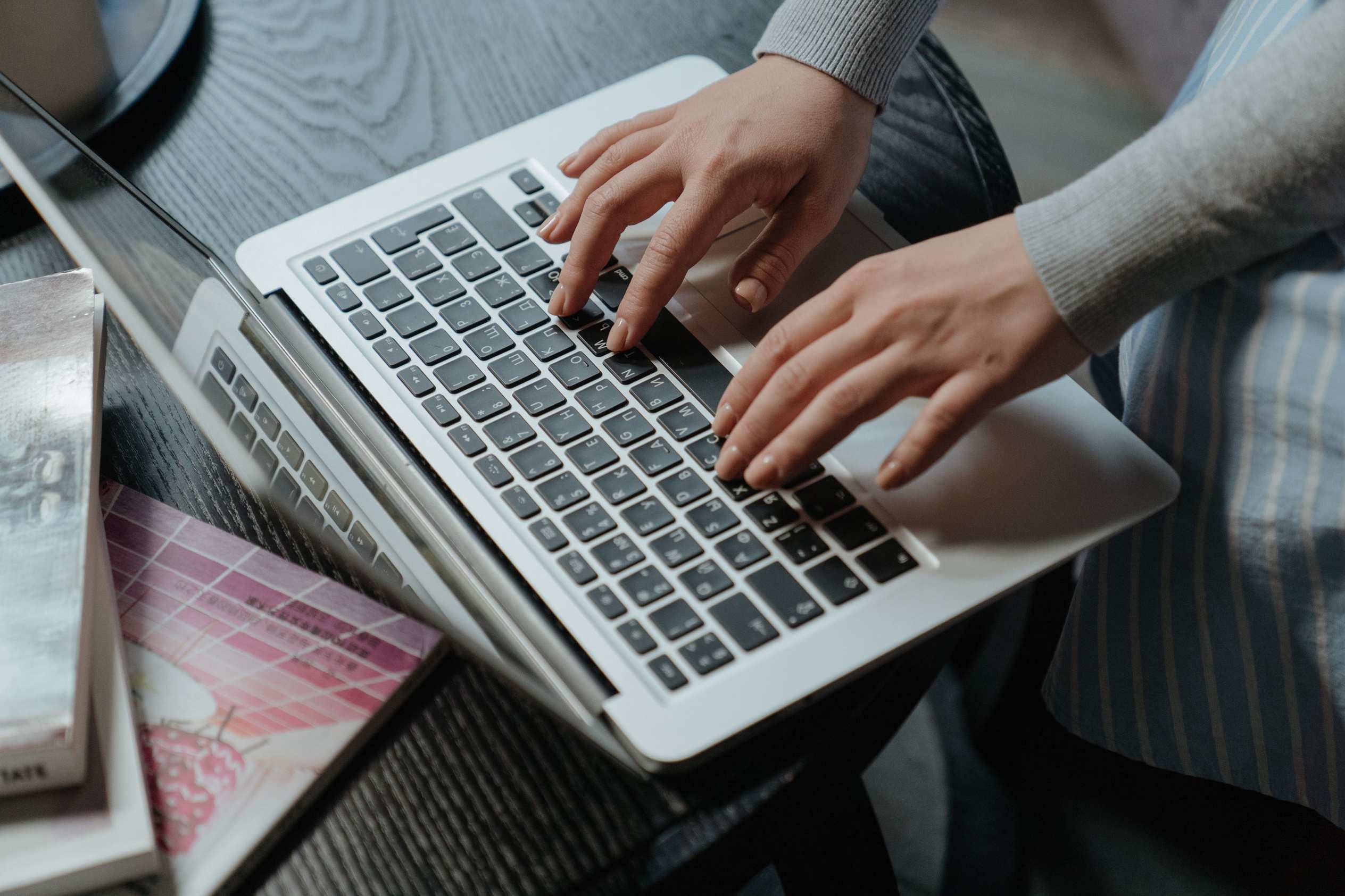 Hands typing on a laptop indoors with books on the table